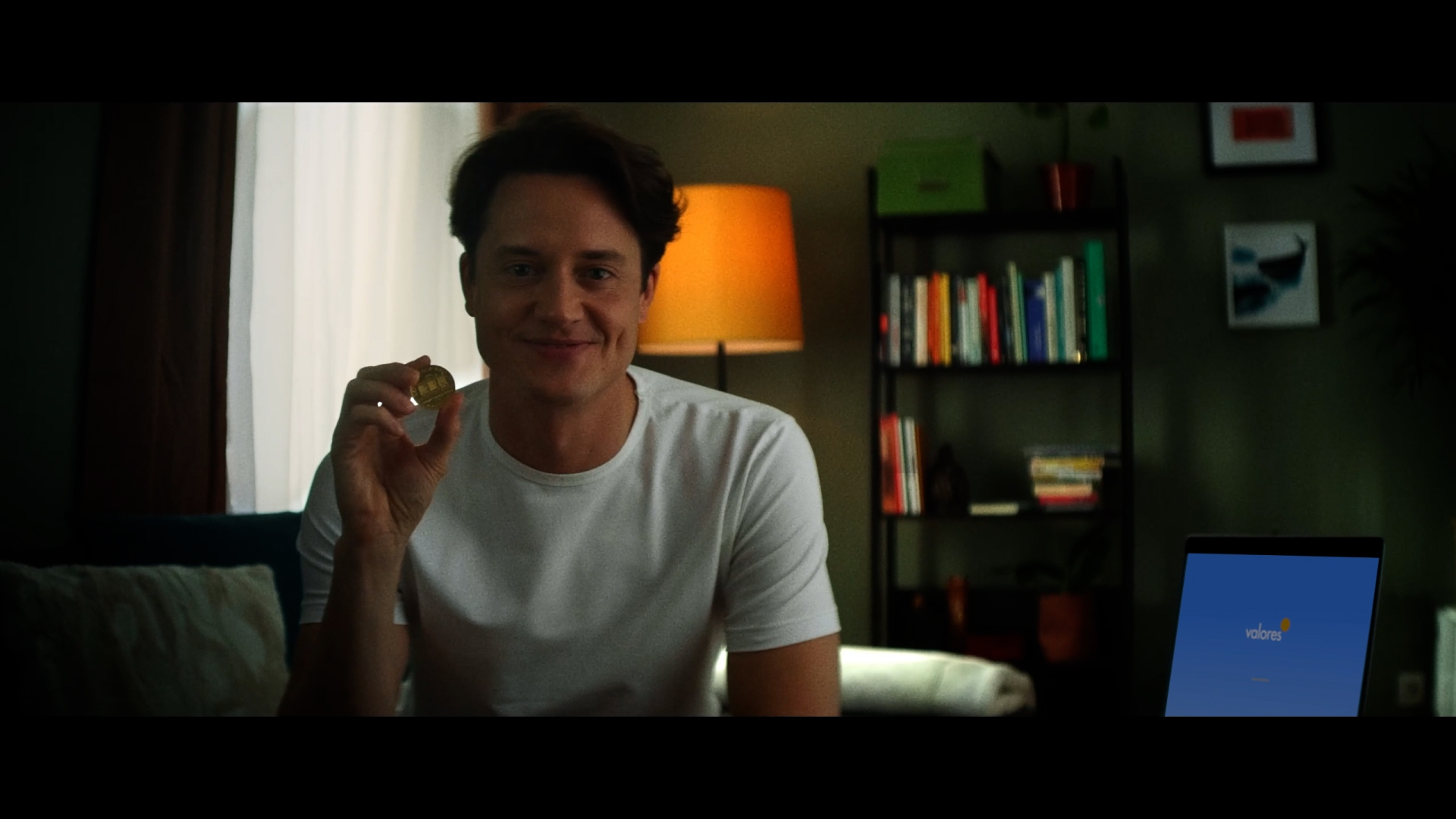 Domen Valič, actor and a celebrity starring in a video advertisement ad, holding a gold coin in hand, explaining the importance of investing in gold.